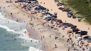 Een druk strand met veel mensen en geparkeerde auto's.