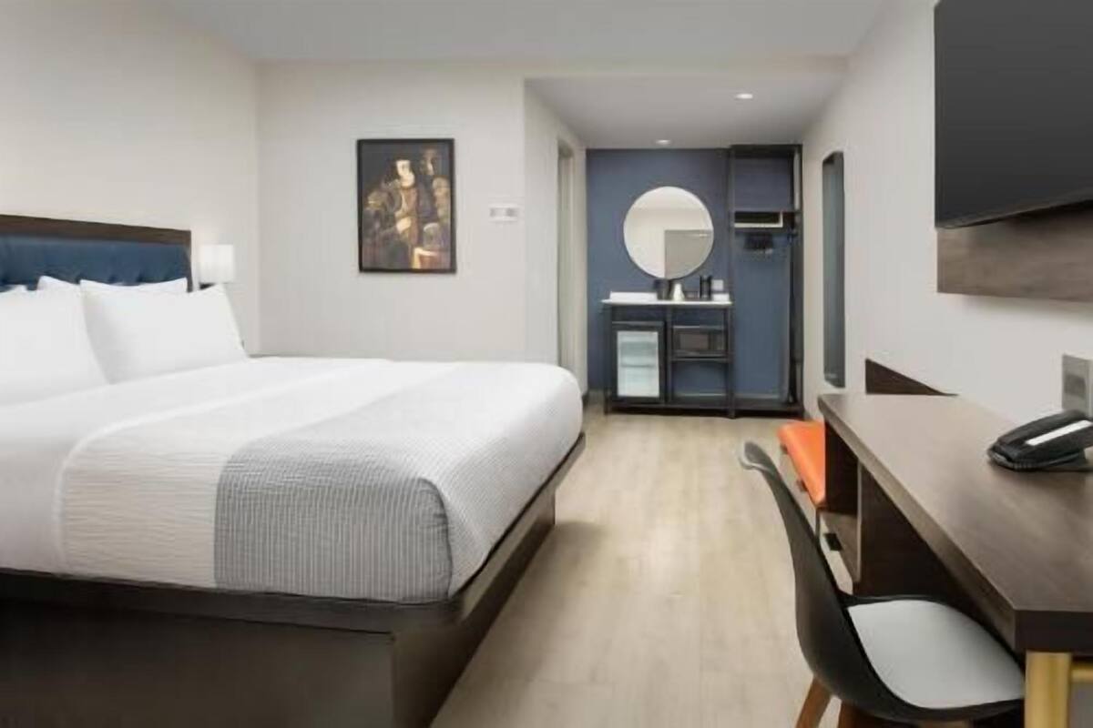 A hotel room with a bed, a desk, a chair, a mirror, and a TV.
