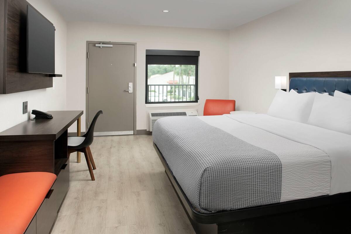 A hotel room with a bed, desk, chair, and a television on the wall.