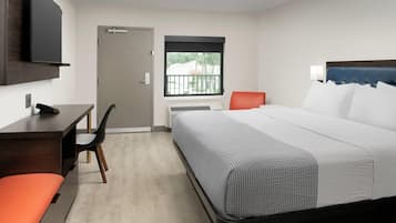 Habitación de hotel con cama, escritorio, silla y televisor en la pared.
