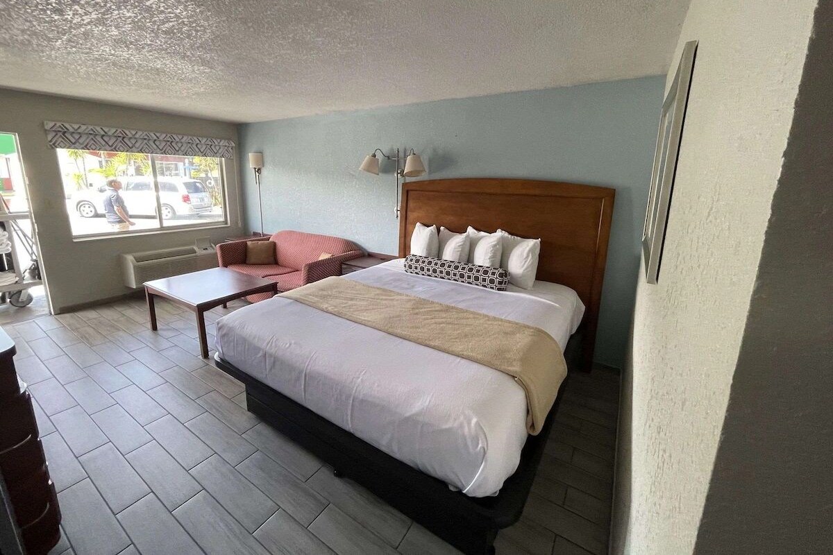Quarto de hotel com uma cama grande, uma mesinha, um sofá e uma janela com vista para a rua.