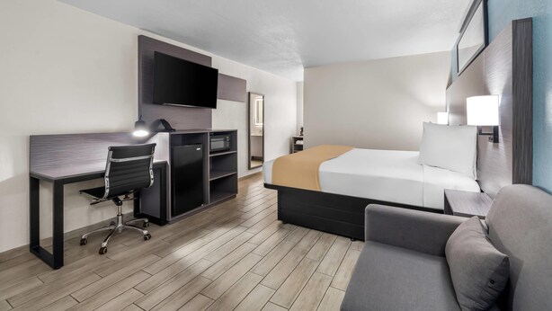 A hotel room with a bed, a desk with a chair, a TV mounted on the wall, and a bedside table with a lamp. - Rodeway Inn Lake Wales - Winter Haven (Lake Wales)