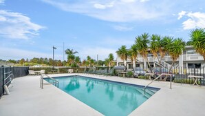 A rectangular swimming pool with a clear blue water surface, surrounded by a concrete deck. There are outdoor seating areas with tables and chairs, and a row of palm trees in the background. - Rodeway Inn Lake Wales - Winter Haven (Lake Wales)