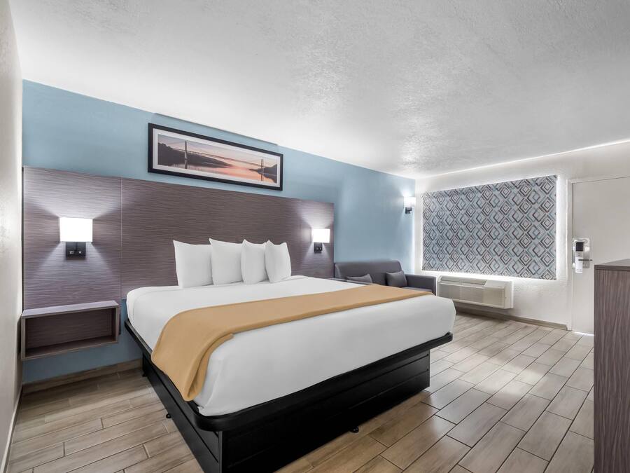 Ein modernes Hotelzimmer mit einem großen Bett, Nachttischen, einem Wand-Fernseher und einem Fenster mit gemusterten Vorhängen.