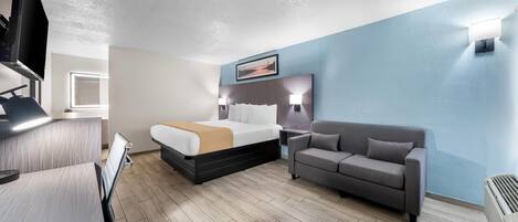 A hotel room with a bed, a sofa, a desk, and a TV.