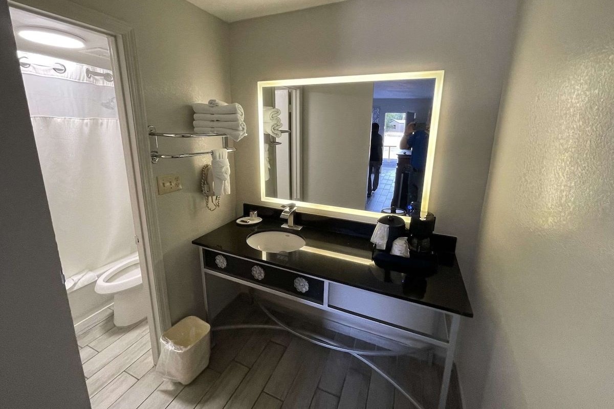 A modern bathroom with a black vanity, a large mirror with LED lighting, a white sink, and a glass shower enclosure.