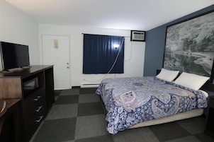 A bedroom with a bed, a desk, a television, a window with curtains, and a painting on the wall.