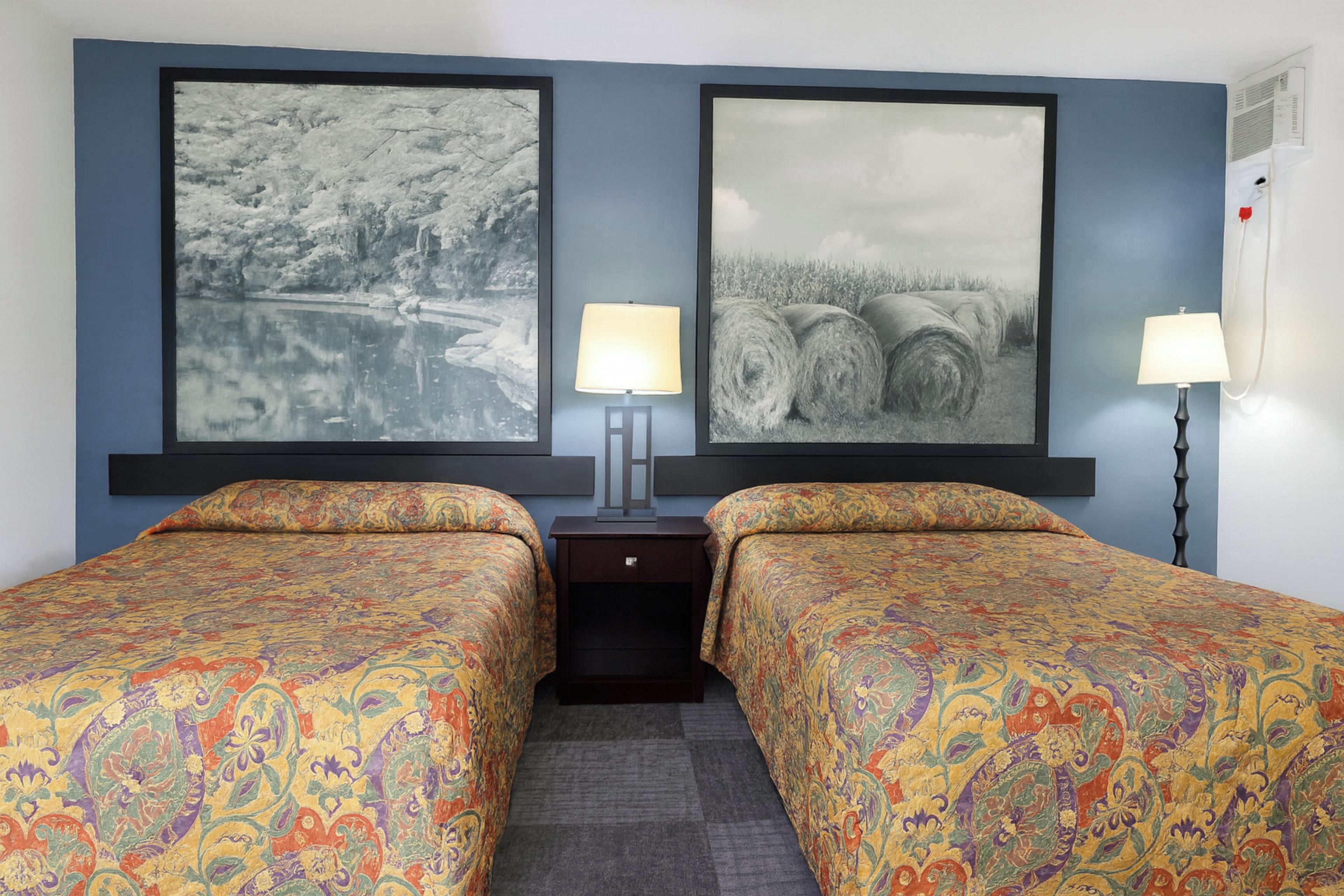 A hotel room with two beds, a nightstand, and two wall-mounted lamps.