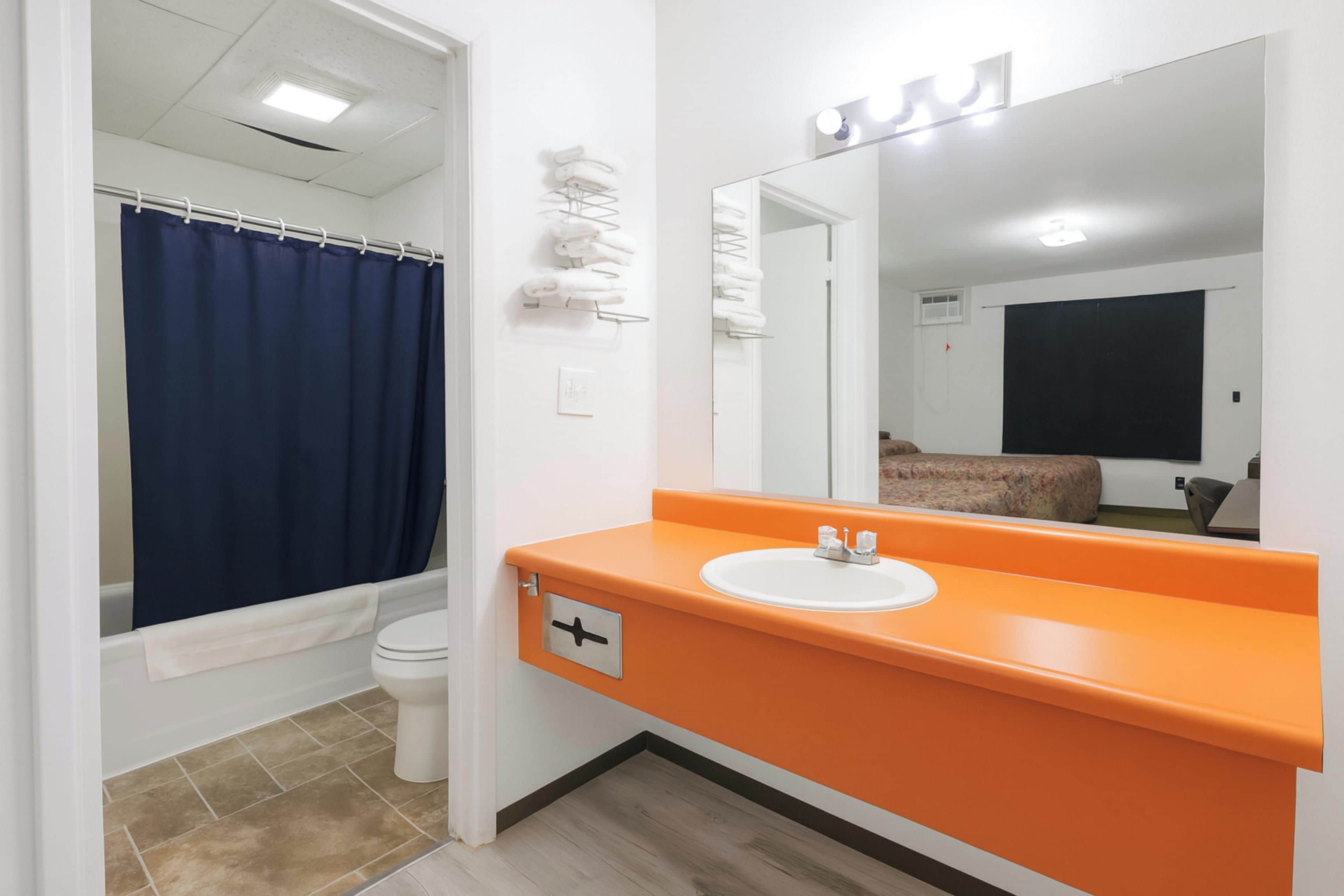 Un baño con inodoro blanco, cortina de ducha azul, lavamanos naranja y un espejo.