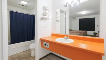 Un baño con inodoro blanco, cortina de ducha azul, lavamanos naranja y un espejo.