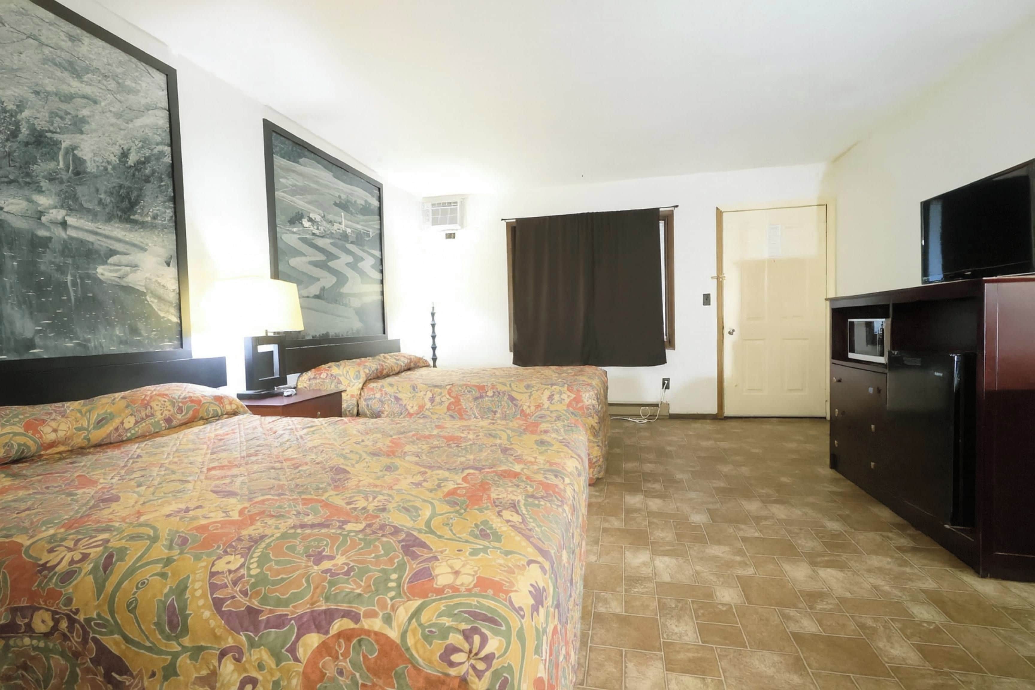 A hotel room with two beds, a television, a desk, and a large painting on the wall.