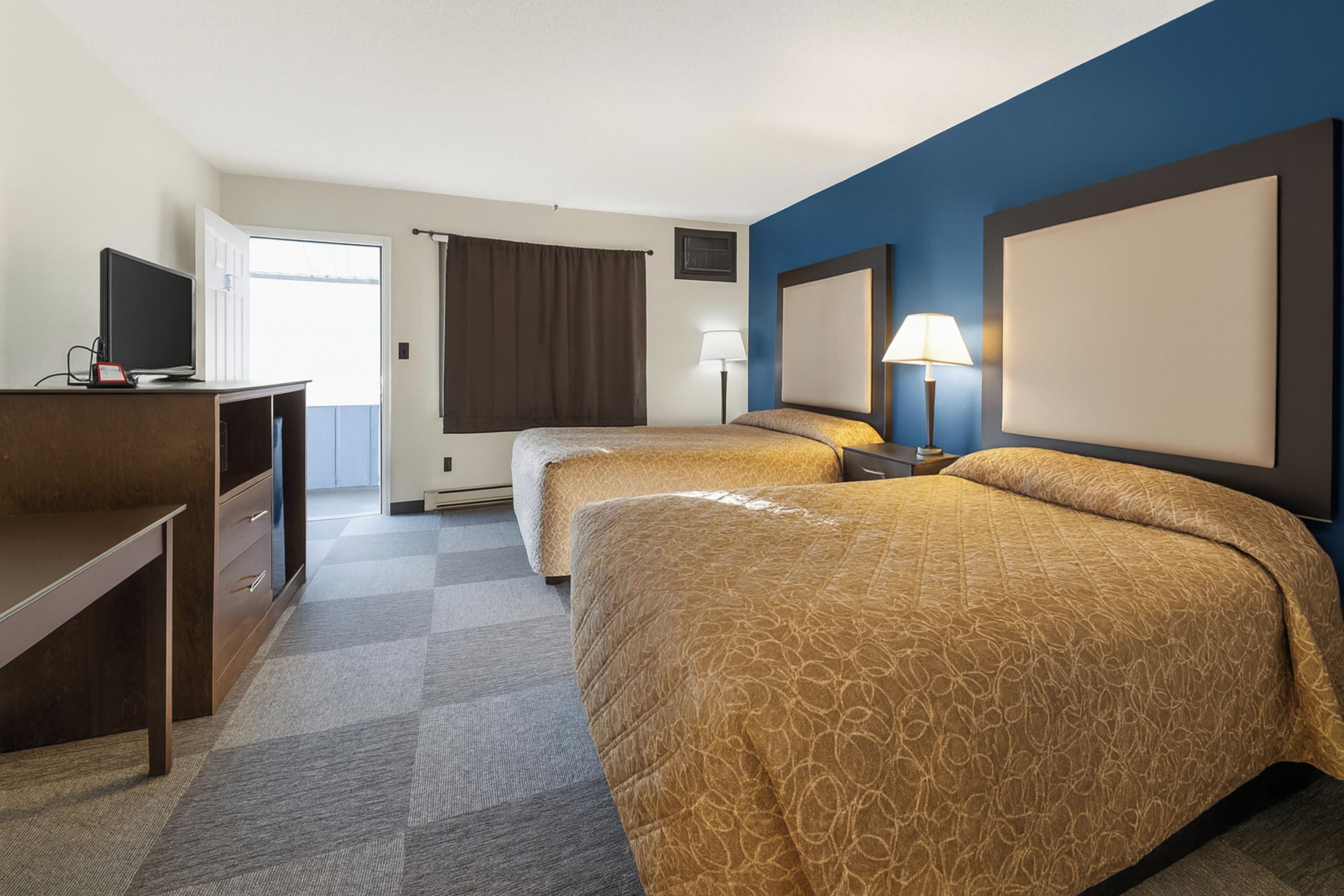 Habitación de hotel con dos camas, un escritorio, un televisor y una ventana con cortinas.