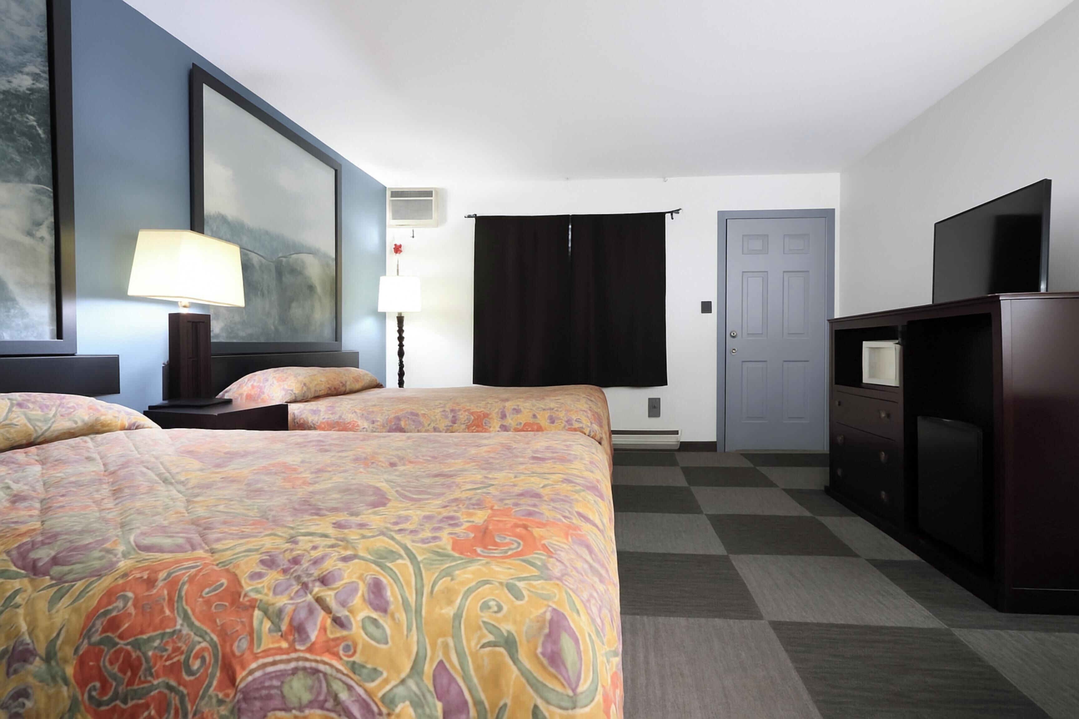 A hotel room with two beds, a television, a desk, and a large painting on the wall.