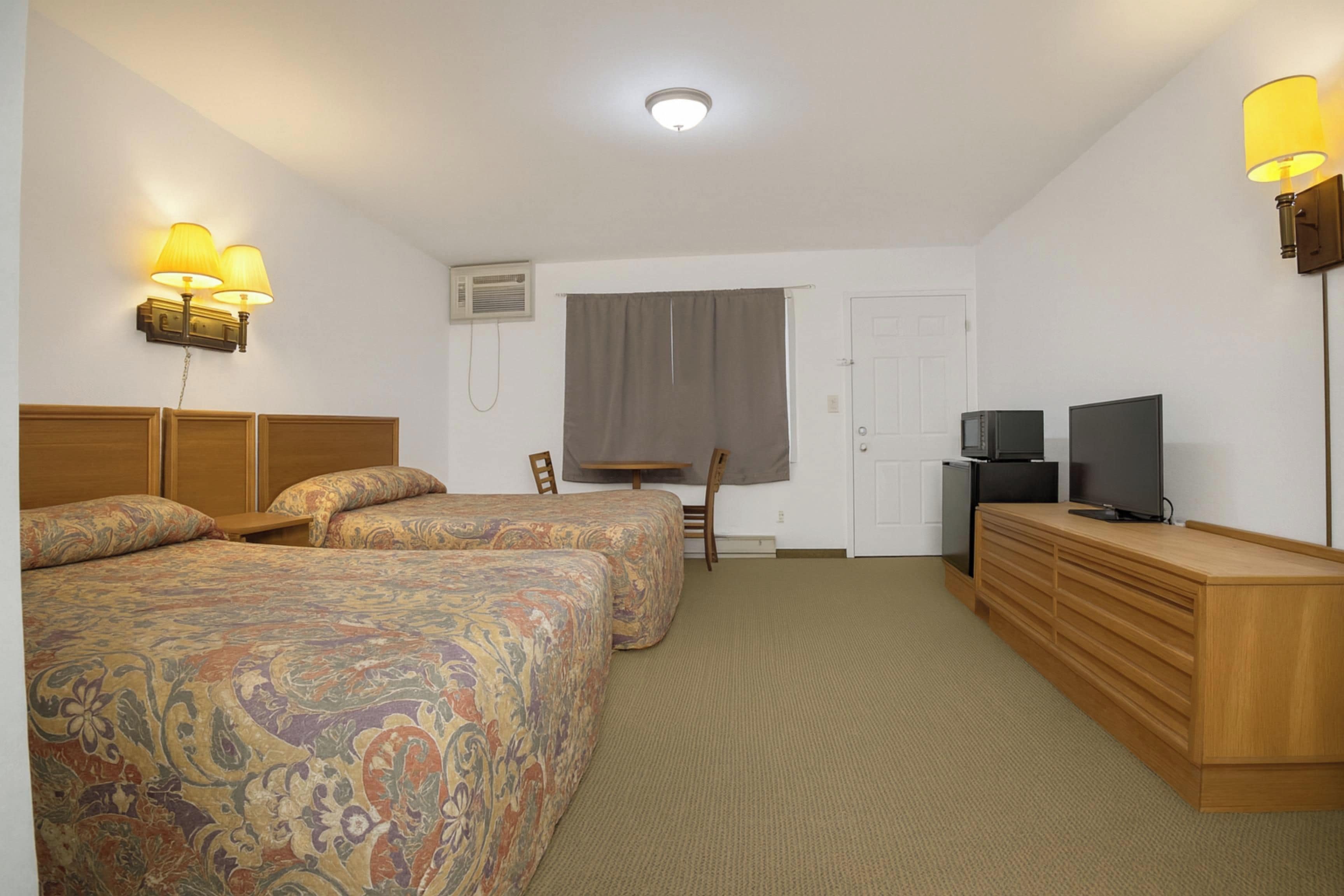 A hotel room with two beds, a desk, a television, and a dresser.