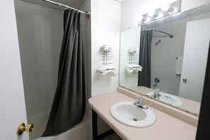 A bathroom with a bathtub, a sink, a mirror, and towel racks. - OYO Landmark Inn Oskaloosa Near Hwy 63 (Oskaloosa)