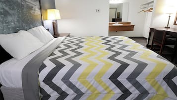 Una habitación de hotel con cama, mesita de noche, lámpara, espejo, escritorio y silla.