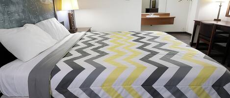 A hotel room with a bed, a nightstand, a lamp, a mirror, a desk, and a chair.