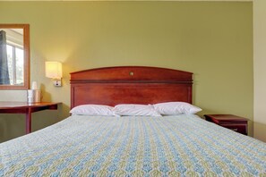 A hotel room with a large bed, a wooden headboard, a bedside table, a lamp, and a mirror. - OYO Landmark Inn Oskaloosa Near Hwy 63 (Oskaloosa)