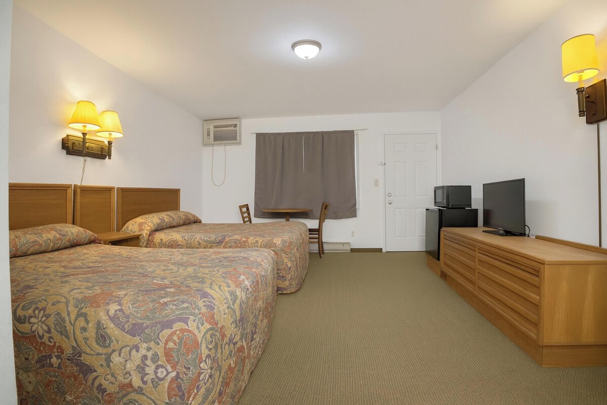 A hotel room with two beds, a desk, a television, and a dresser.