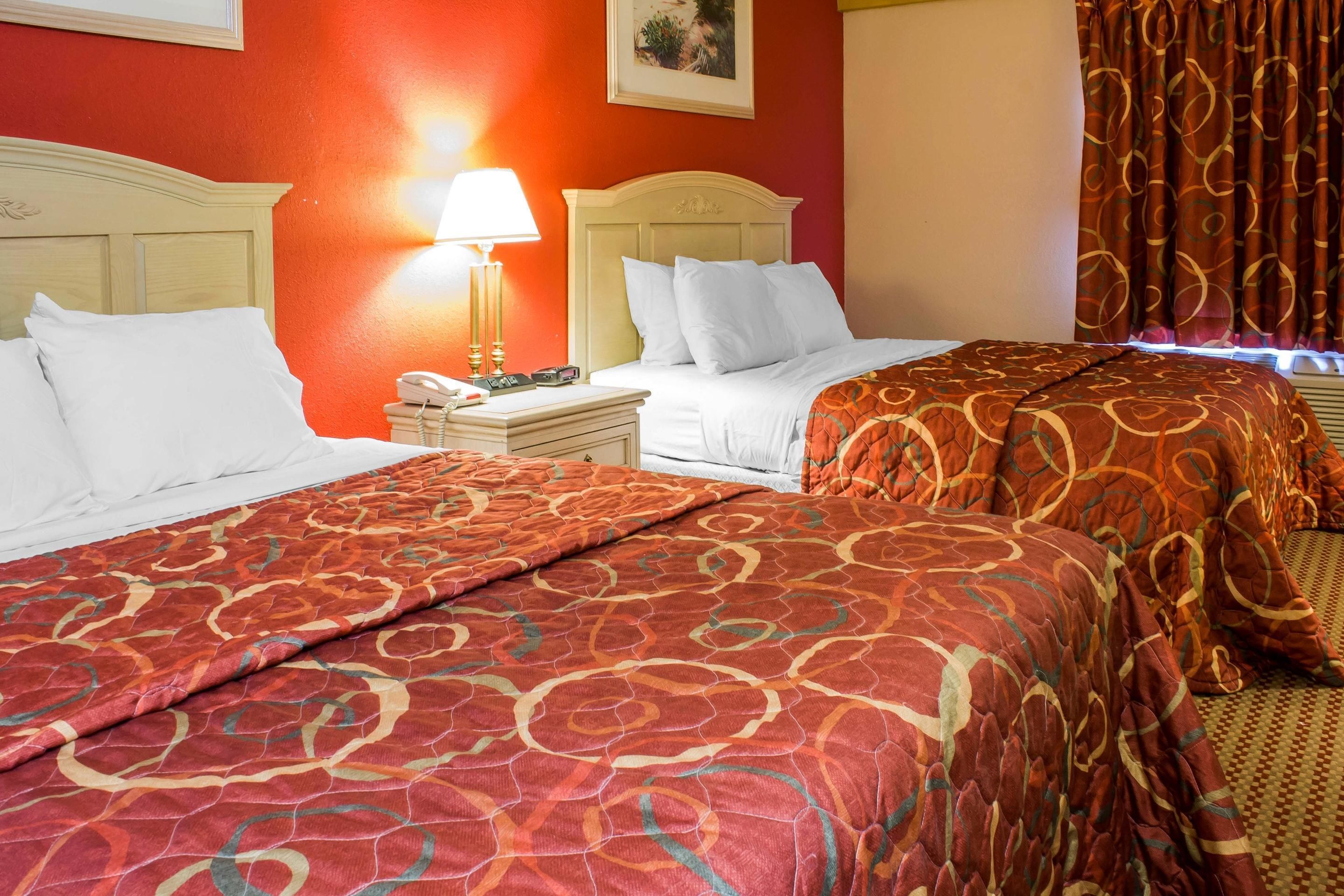 Een hotelkamer met twee bedden, een nachtkastje met een lamp en een rode wand.