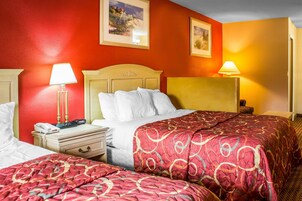 Habitación de hotel con dos camas, una mesita de noche con lámpara y un cuadro en la pared.