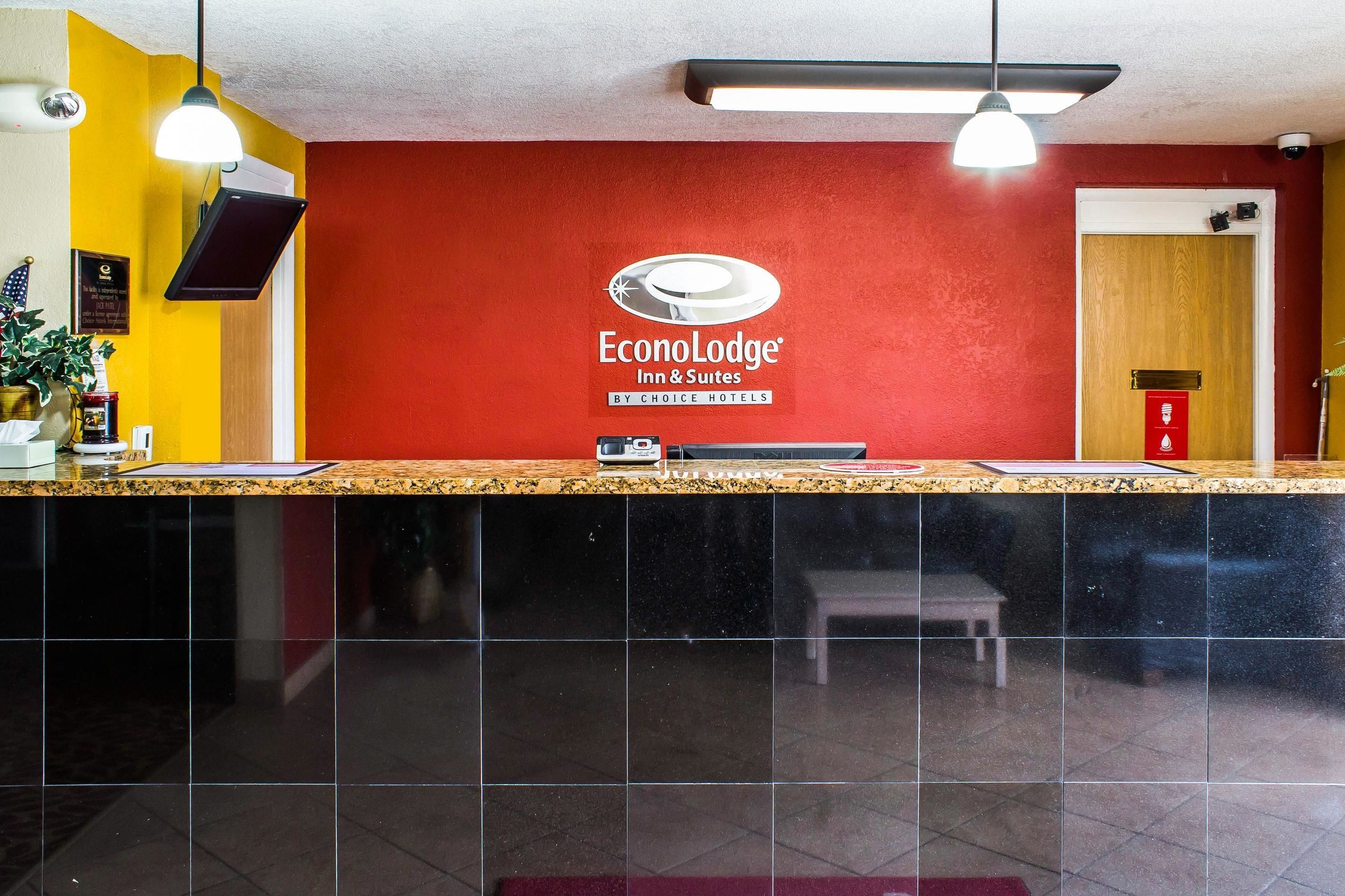 A reception area with a red wall, a sign for EconoLodge Inn & Suites, a reception desk, and a bench.