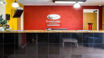 A reception area with a red wall, a sign for EconoLodge Inn & Suites, a reception desk, and a bench.