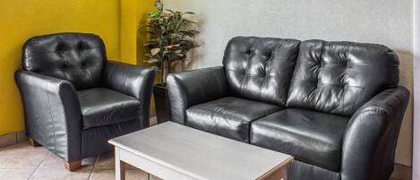 A room with a black leather sofa, a matching armchair, and a small white table.