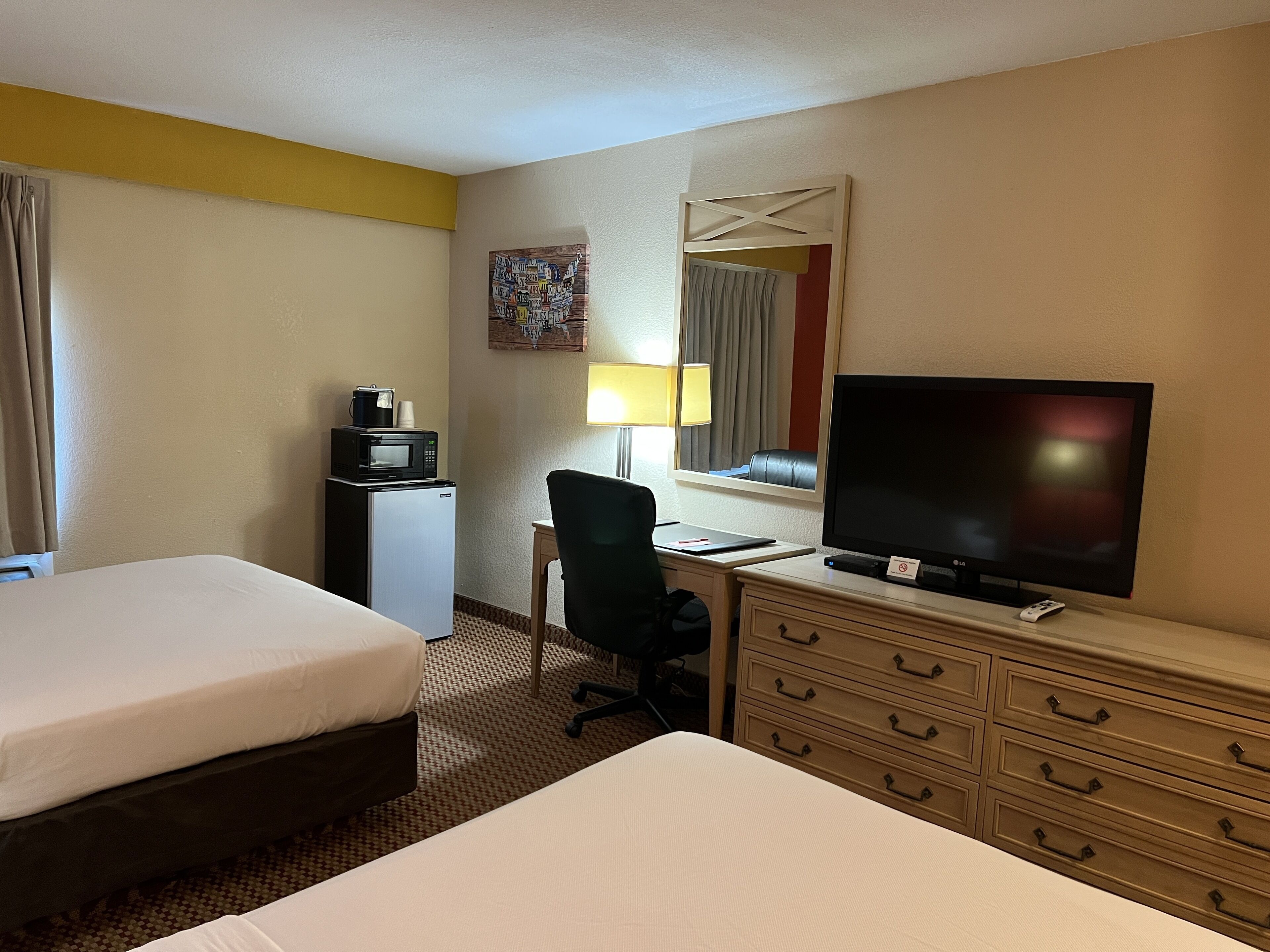 Et hotelværelse med to senge, et skrivebord med computer, tv, mikroovn og et lille køleskab.