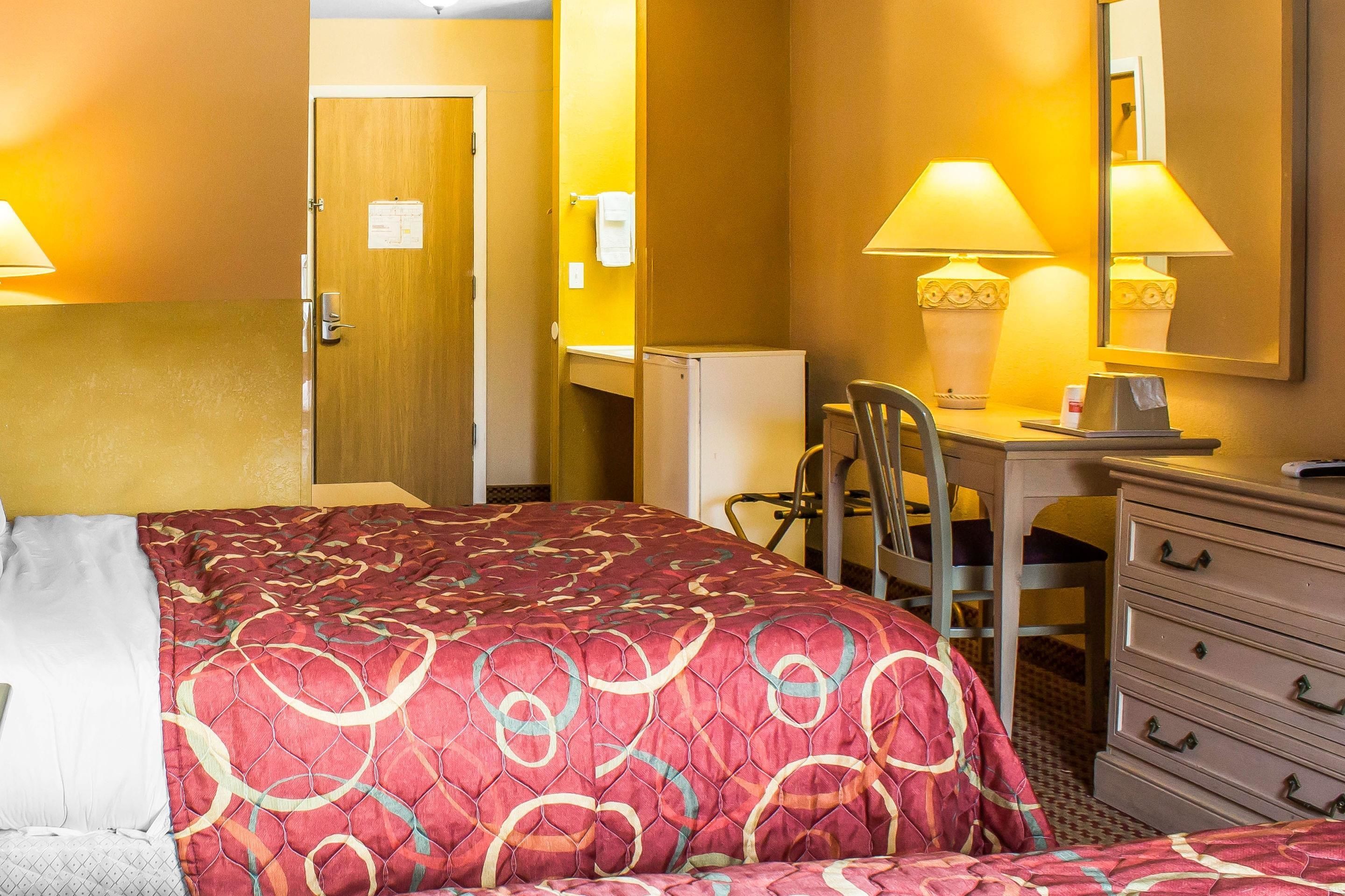 A hotel room with a large bed, a desk with a chair, a dresser, and a mirror.