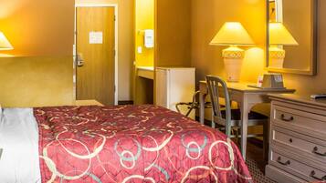 A hotel room with a large bed, a desk with a chair, a dresser, and a mirror.