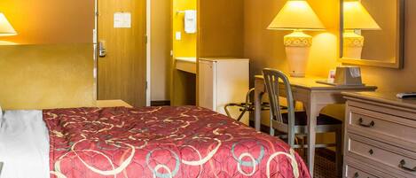 A hotel room with a large bed, a desk with a chair, a dresser, and a mirror.