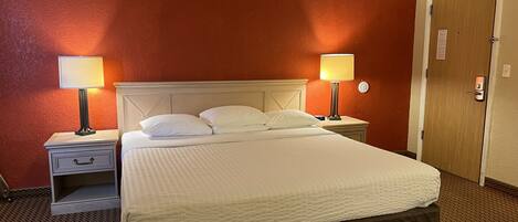 A hotel room with a single bed, two bedside tables with lamps, a wooden door, and a red wall.