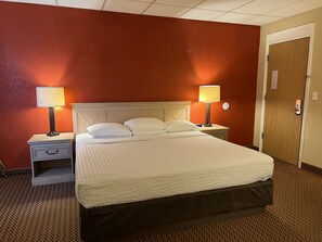 A hotel room with a single bed, two bedside tables with lamps, a wooden door, and a red wall.