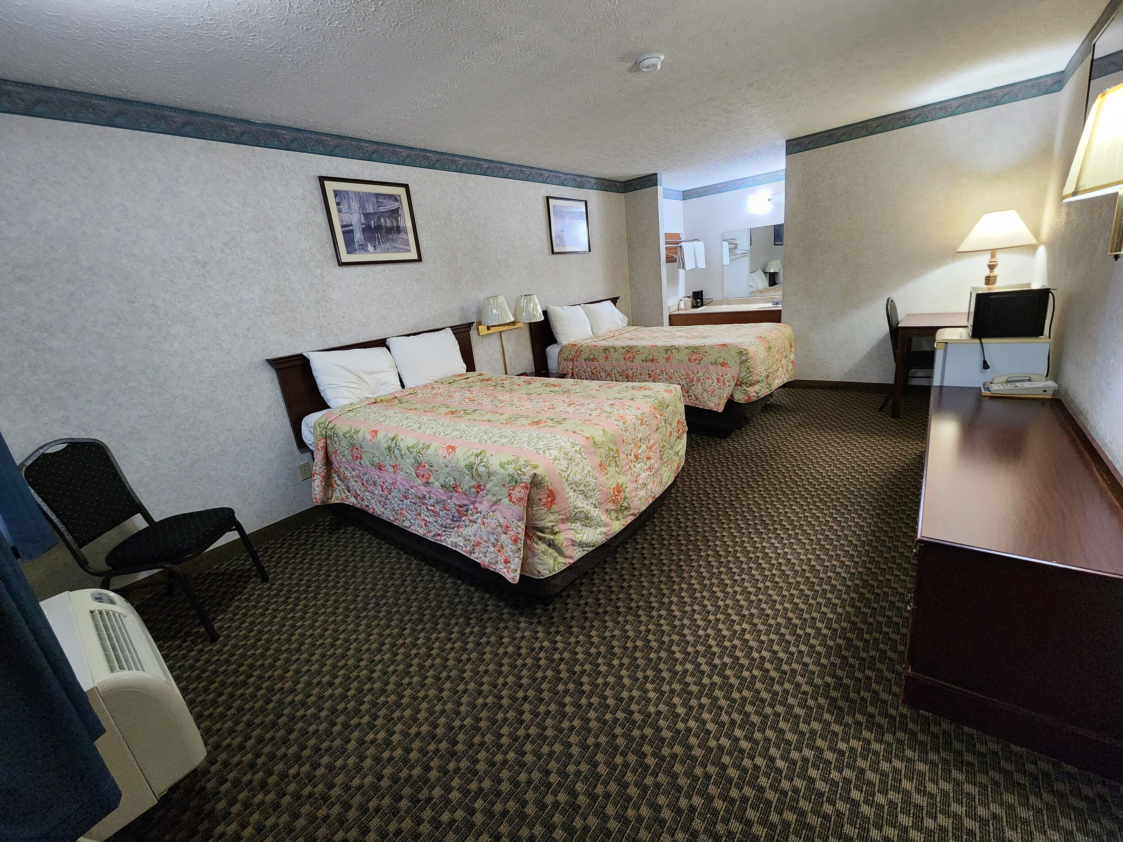 Une chambre d’hôtel avec deux lits, un bureau, une chaise, une lampe et un téléphone.