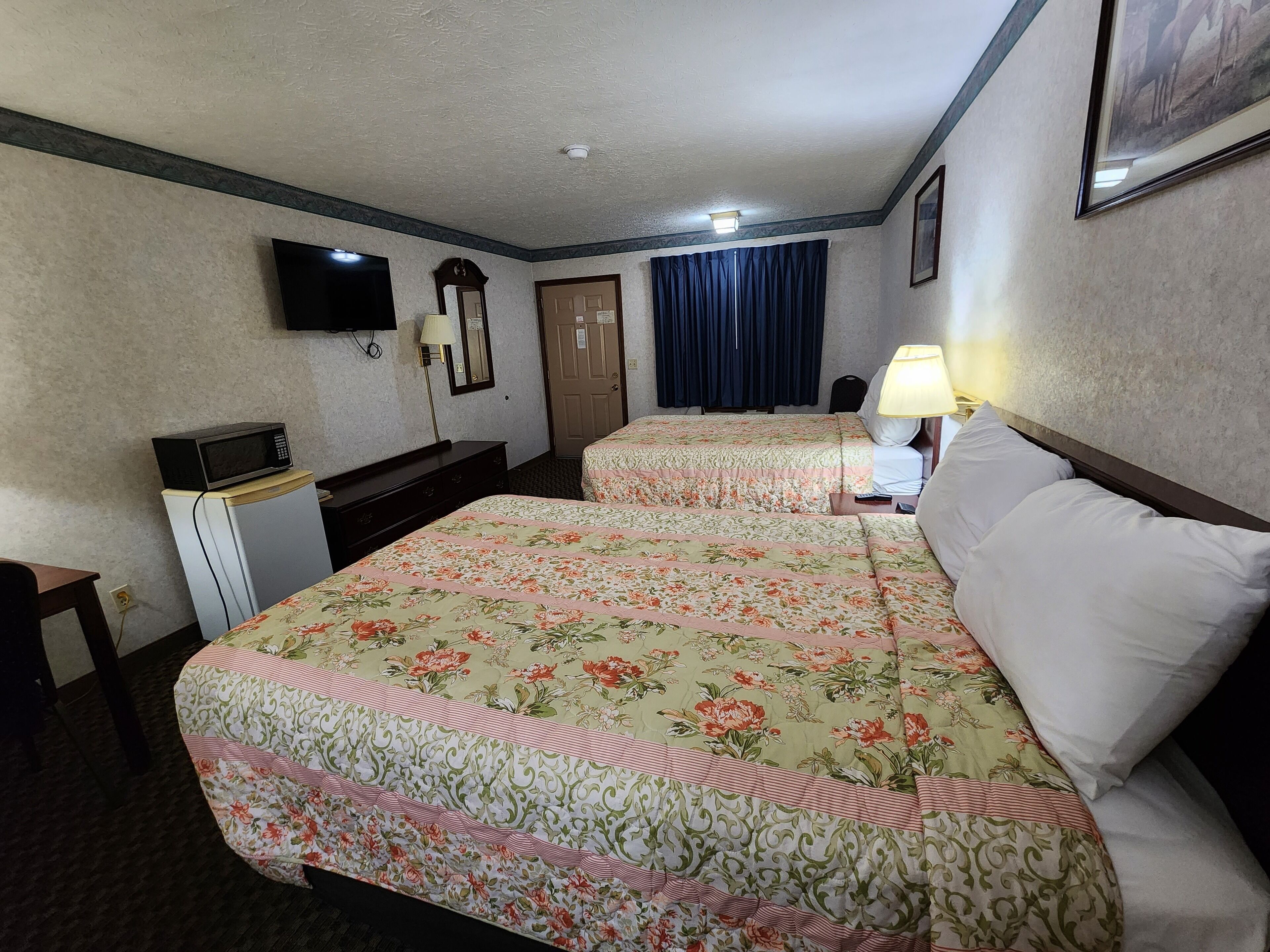 A hotel room with two beds, a desk, a television, and a lamp.