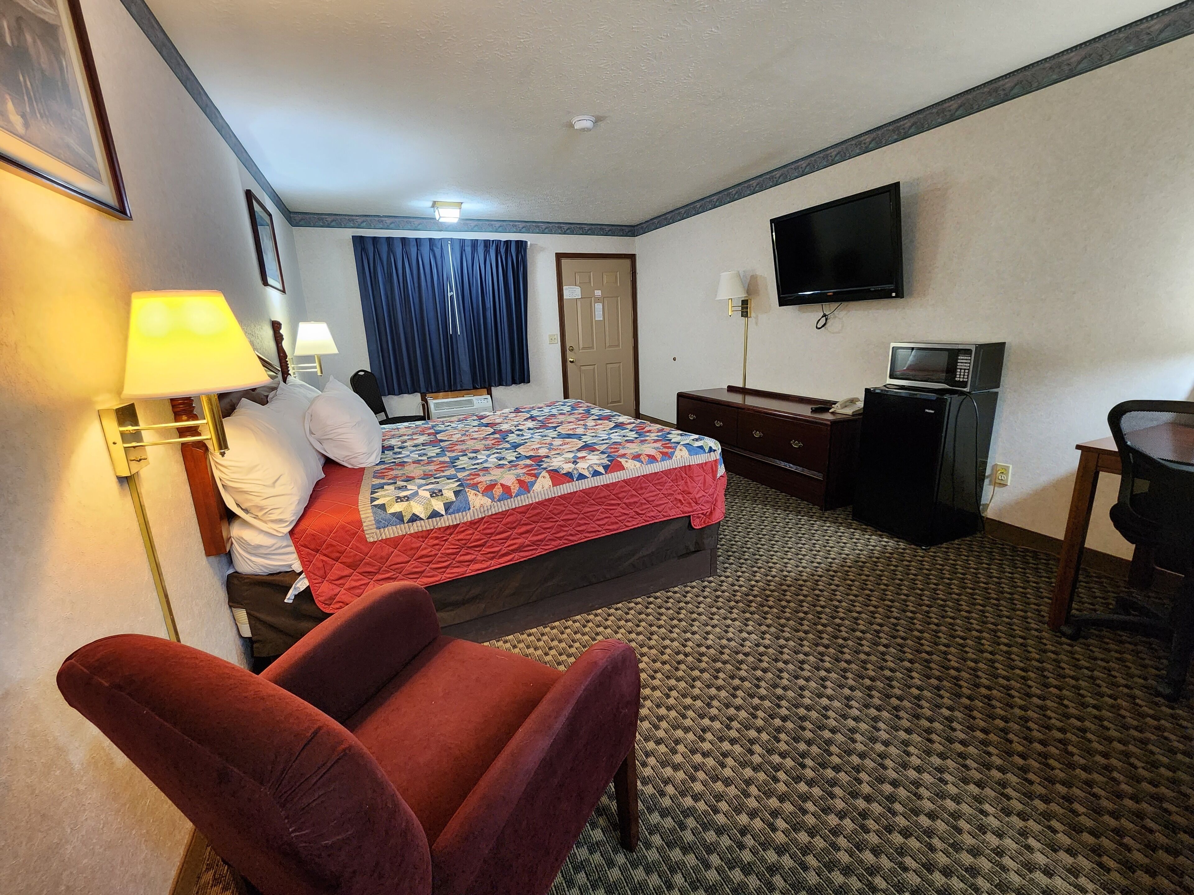 Een hotelkamer met een bed, een bureau, een televisie, een magnetron en een rode stoel.