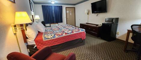 Een hotelkamer met een bed, een bureau, een televisie, een magnetron en een rode stoel.