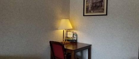 A small table with a lamp, a framed picture on the wall, and a chair.