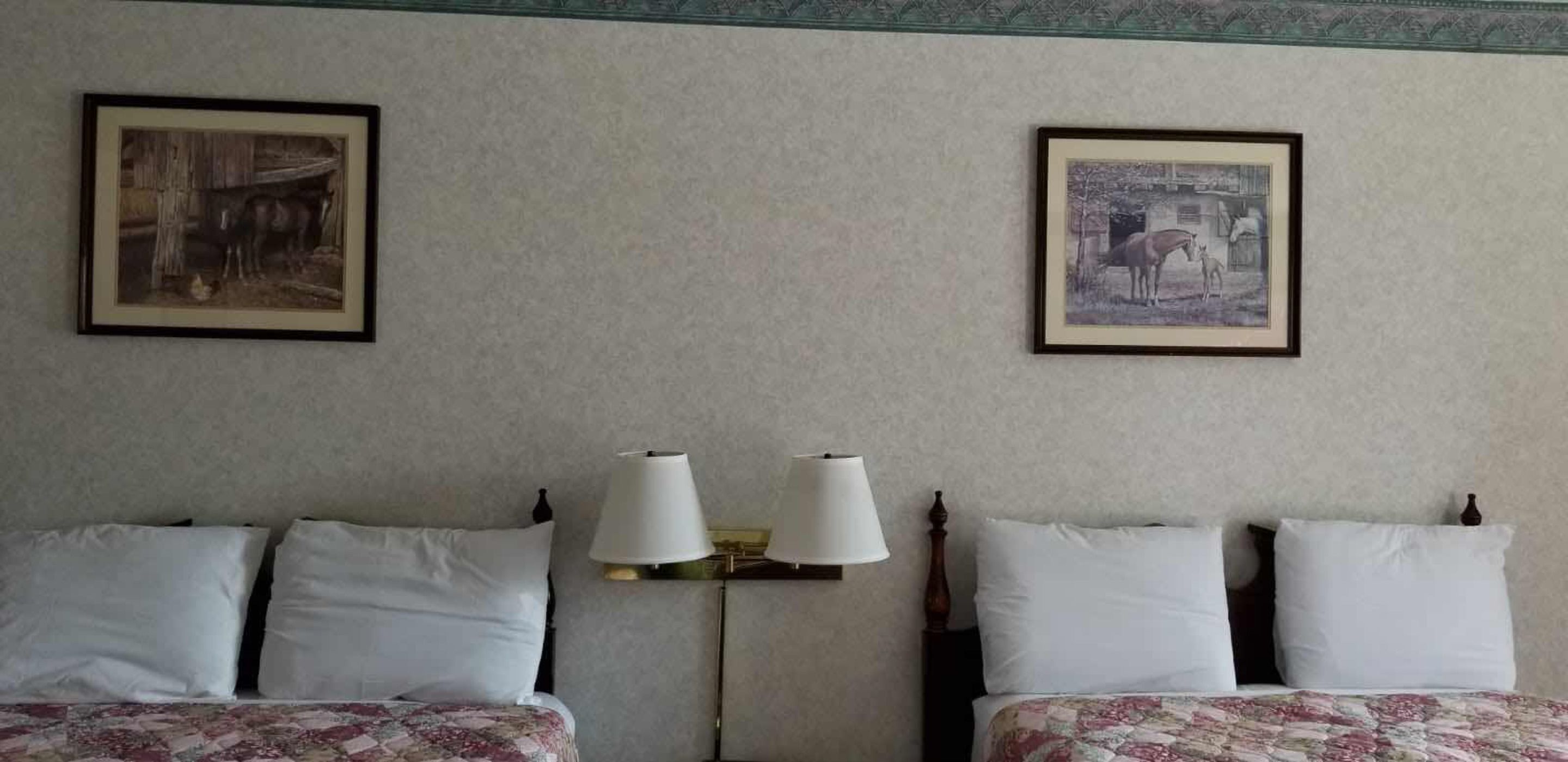 Habitación de hotel con dos camas, cada una con sábanas blancas y mantas de estampado floral. Entre las camas hay dos lámparas fijadas a la pared.