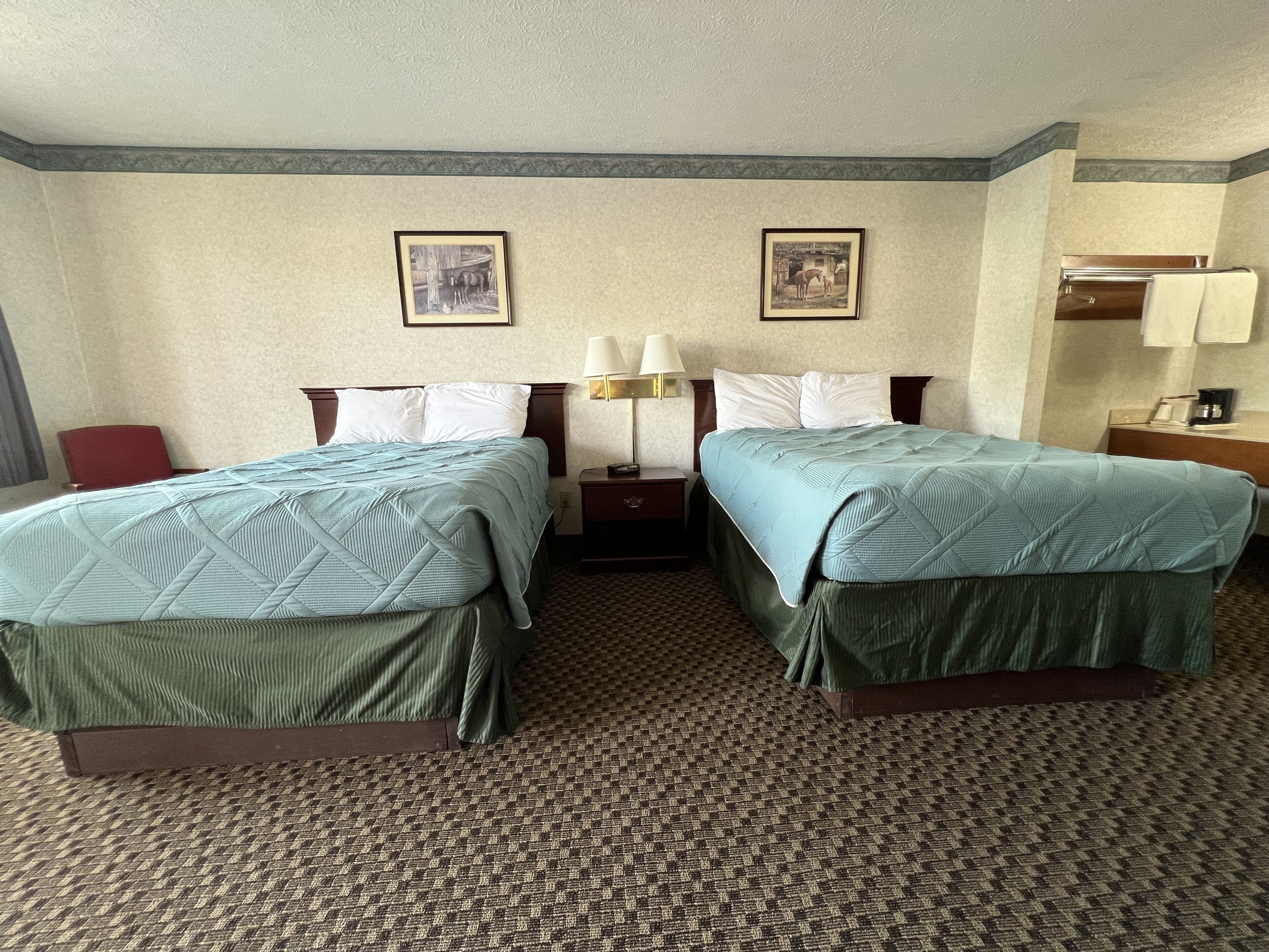 A hotel room with two beds, a nightstand with a lamp, and two framed pictures on the wall.