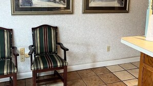 Quarto com duas pinturas emolduradas, uma cadeira listrada e uma mesa pequena.