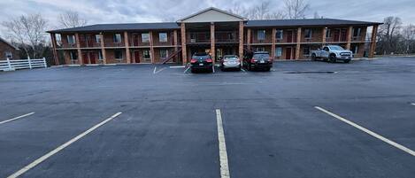 A large parking lot with multiple cars parked in front of a multi-story building with a brick facade and a covered entrance.