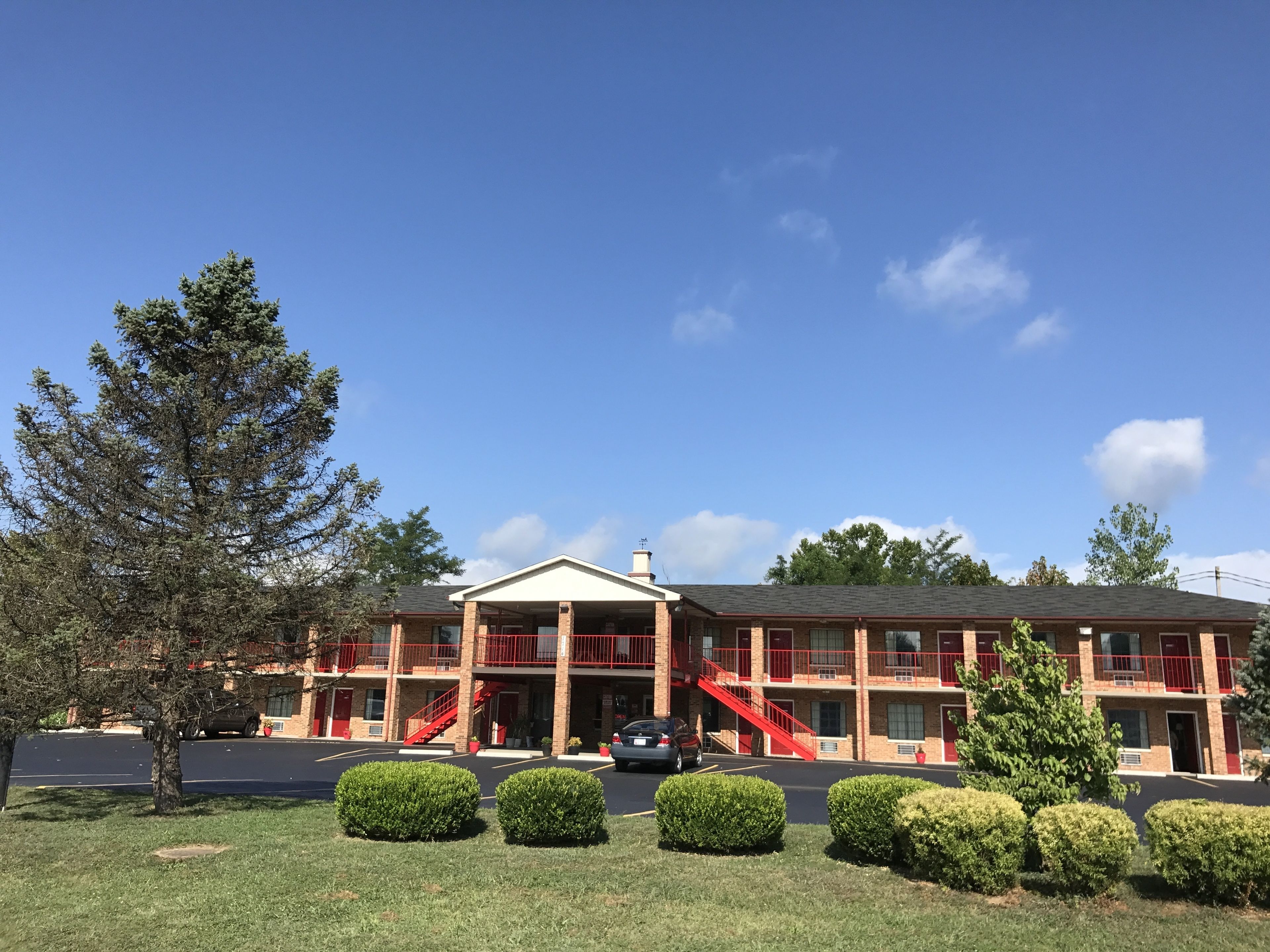 A two-story motel with a red exterior, multiple balconies, and a parking lot.