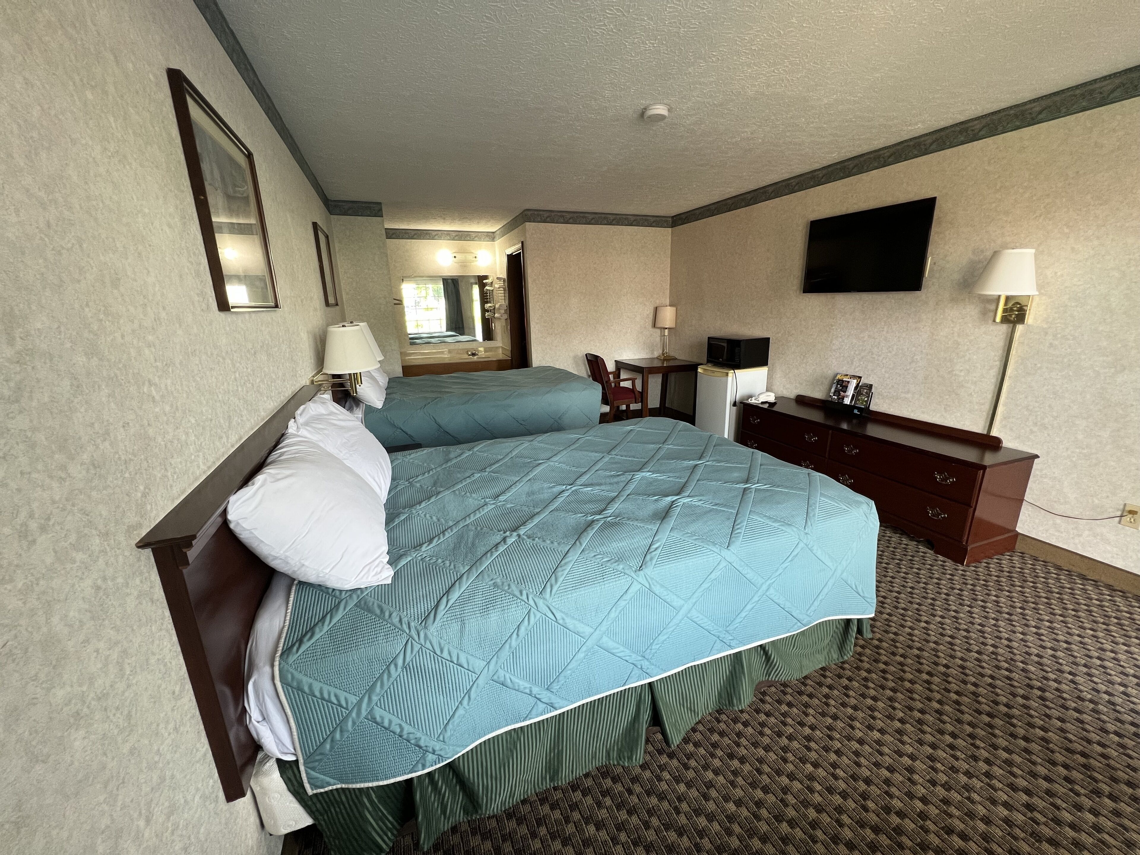 A hotel room with a large bed, a desk, a chair, a television, and a dresser.