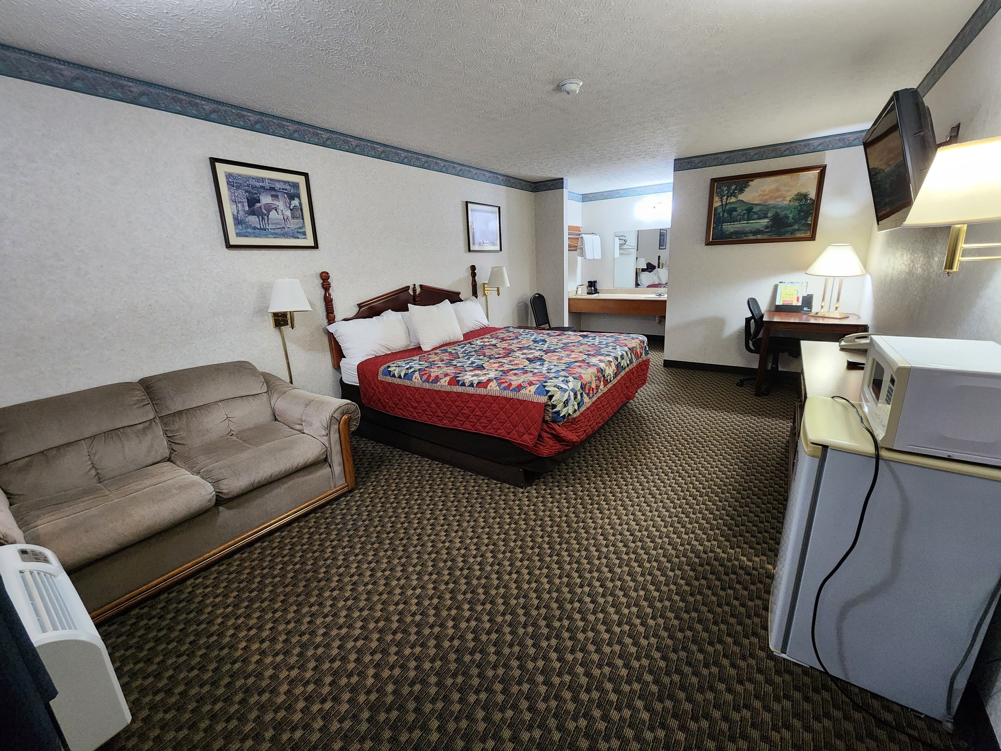 A hotel room with a bed, a couch, a desk, a microwave, and a television.