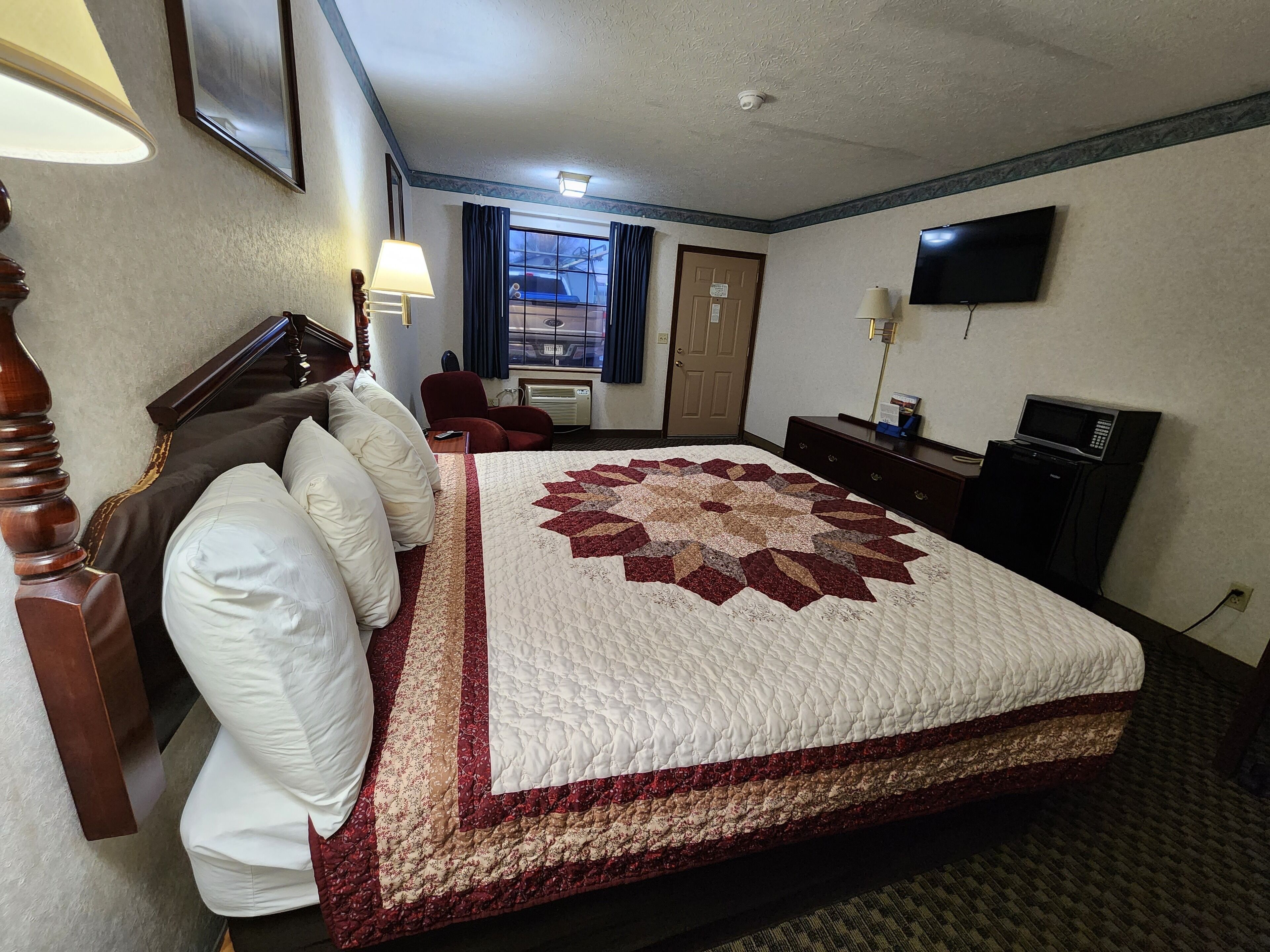 A hotel room with a large bed, a desk, a chair, a television, and a window with curtains.