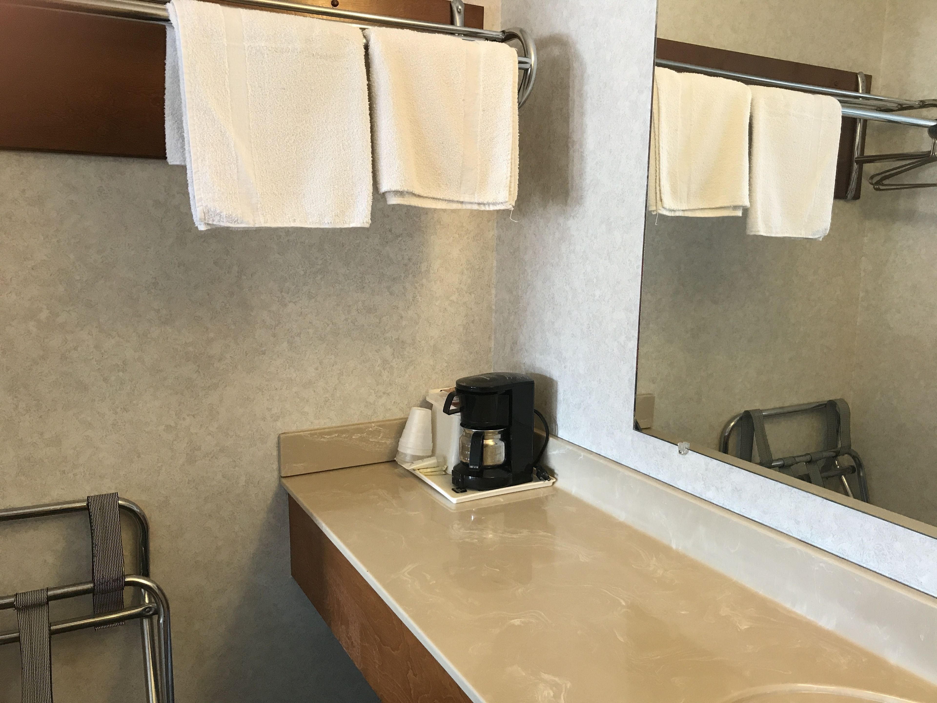 Een badkamer met een beige aanrecht, een koffiezetapparaat en een handdoekhouder met twee handdoeken.