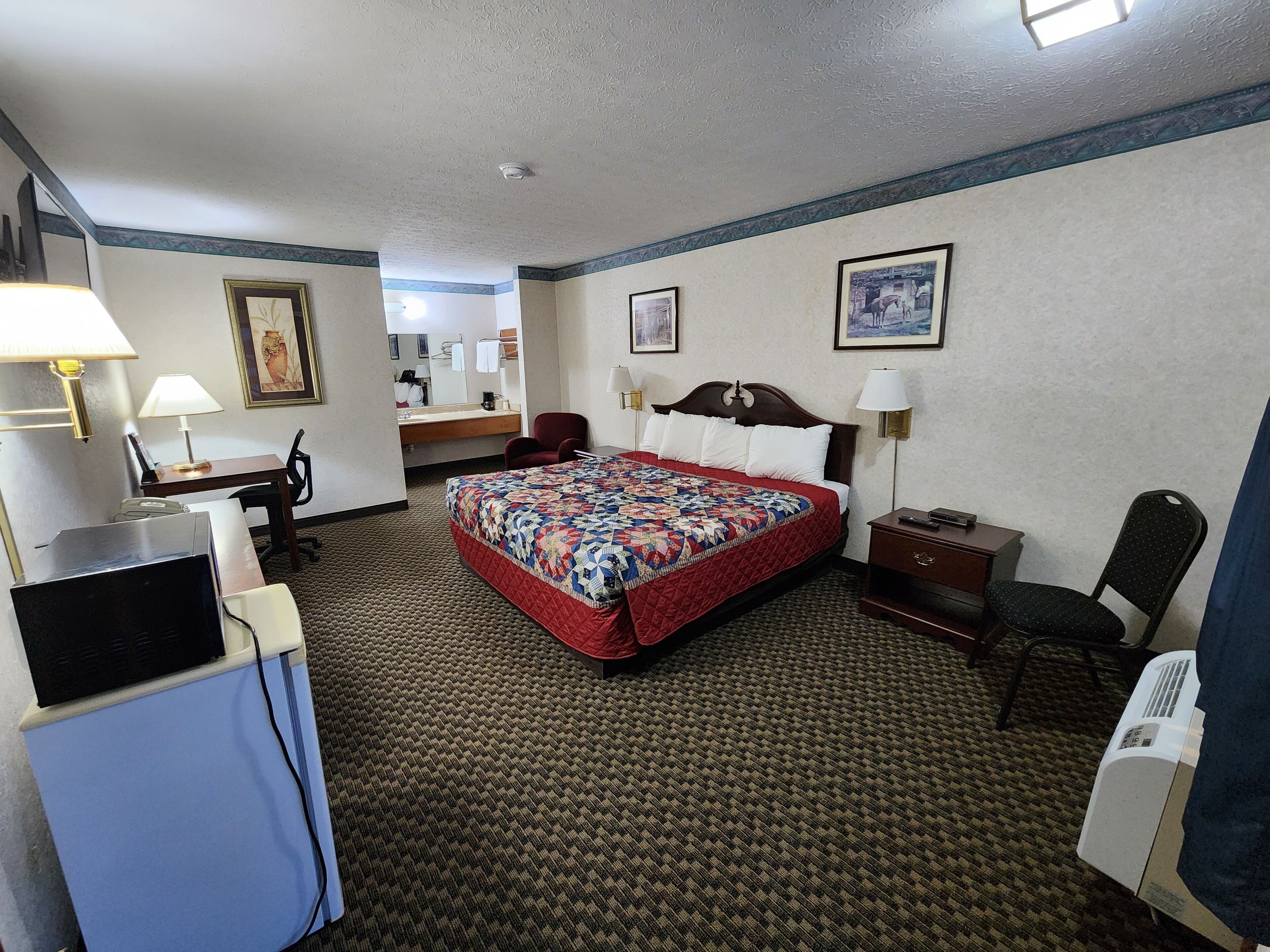 A hotel room with a bed, desk, chair, and a desk lamp.