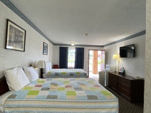 A hotel room with a large bed, a desk, a television, and a view of the outdoors.